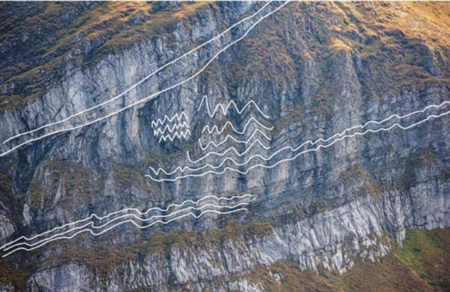 The photograph shows a grass-covered rock with white lines drawn on it, indicating thrusts—some simple, others more complex.