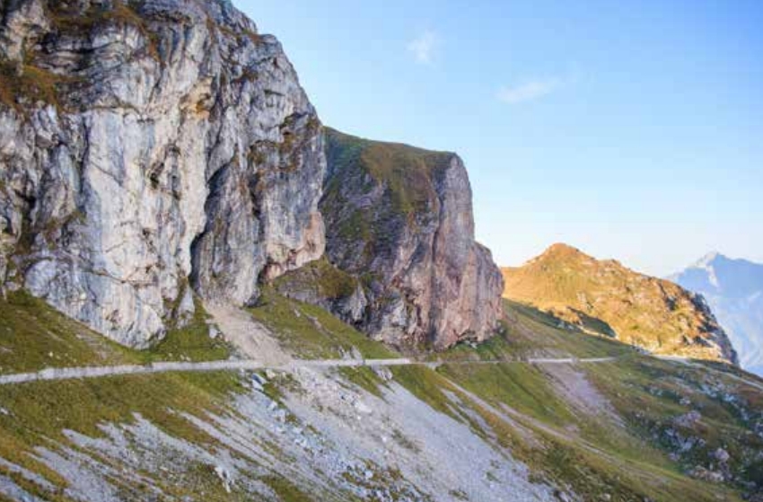 The photograph shows a steep, quarry-like terrain covered with grass. At the top runs a path, above which rocks rise.
